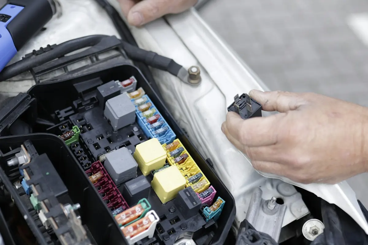 Técnico trabajando con una herramienta sobre la caja de fusibles de un vehículo.