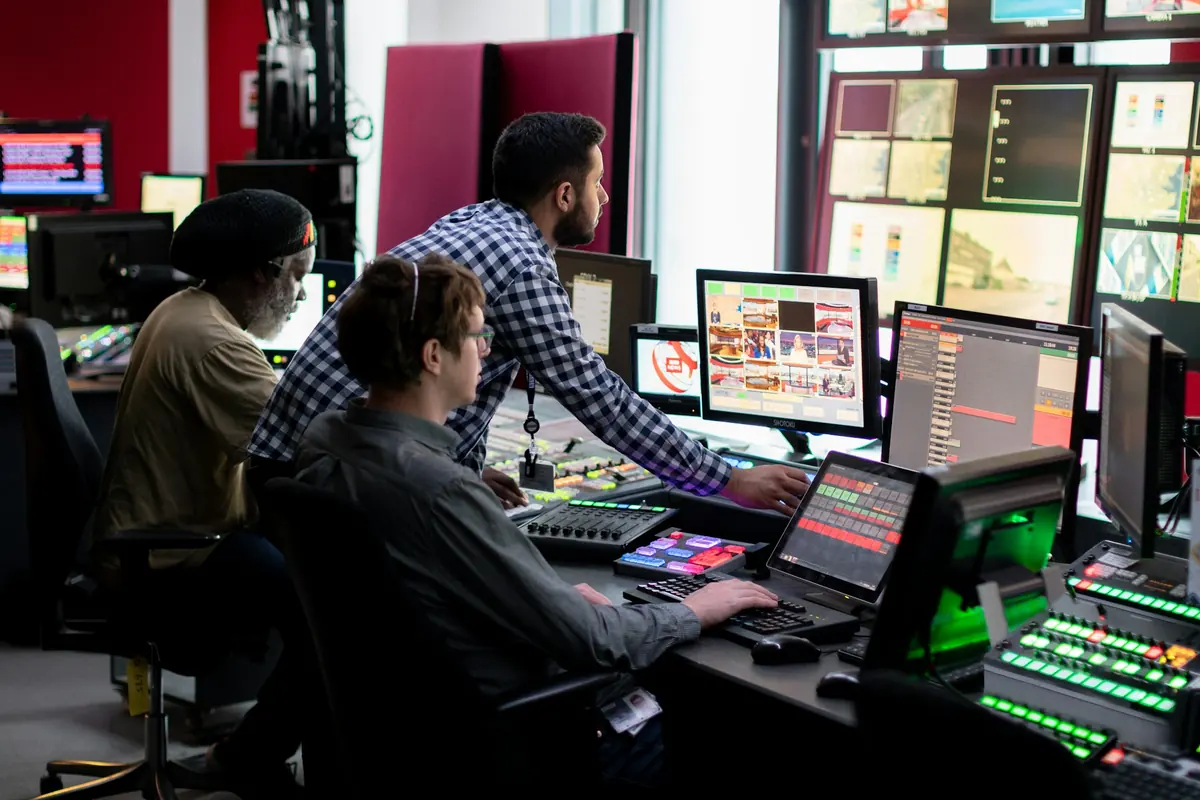 Operadores trabajando en consolas frente a un muro de pantallas en una sala de control moderna.